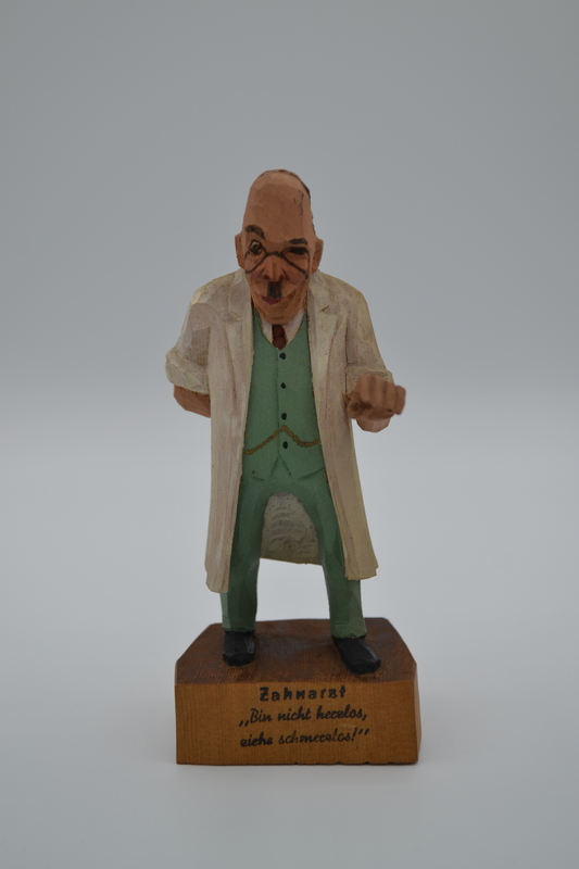 A wood figurine of dentist, holding tooth extracting forceps behind his back,  with inscription: "I'm not heartless, I pull painless" in German