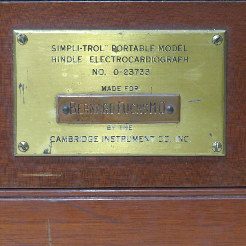 A wooden case with a handle and a brass plaque inscribed: "Made for Bernard Fuchs MD." Case contains portable electrocardiograph. Unlike earlier battery powered photographic models, this is an AC powered instrument.