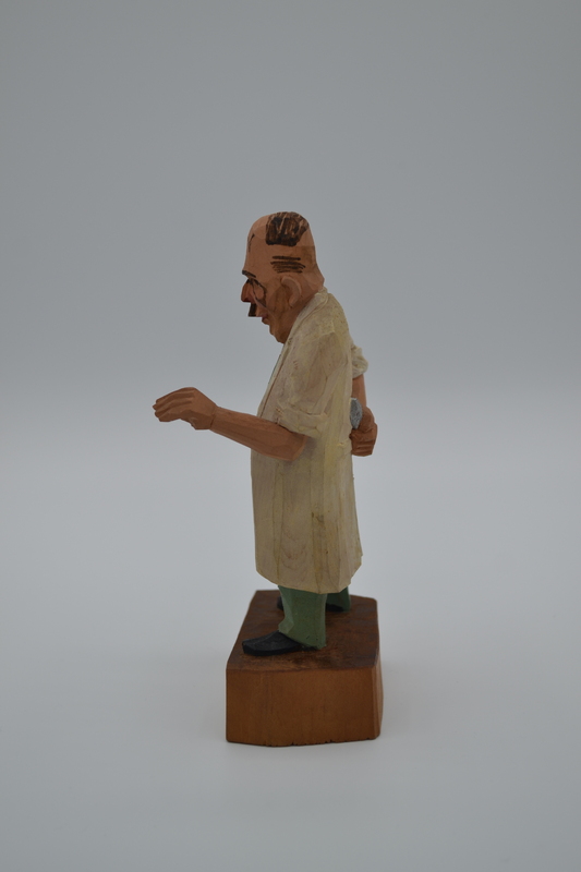 A wood figurine of dentist, holding tooth extracting forceps behind his back,  with inscription: "I'm not heartless, I pull painless" in German