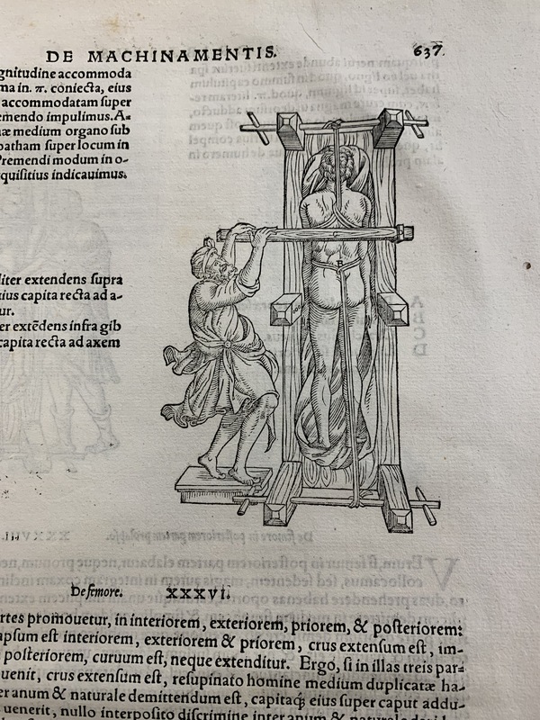 A photo of an old book, open to a page showing Latin text and an illustration of a person in a wooden device with ropes attached to them.
