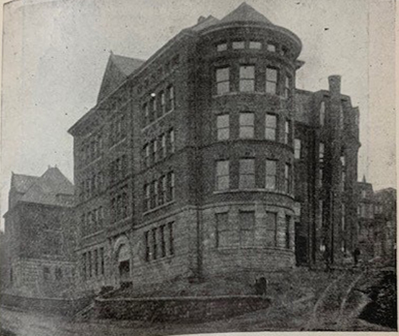 Black-and-white, grainy picture of a four-story brick building with a round addition to its front.