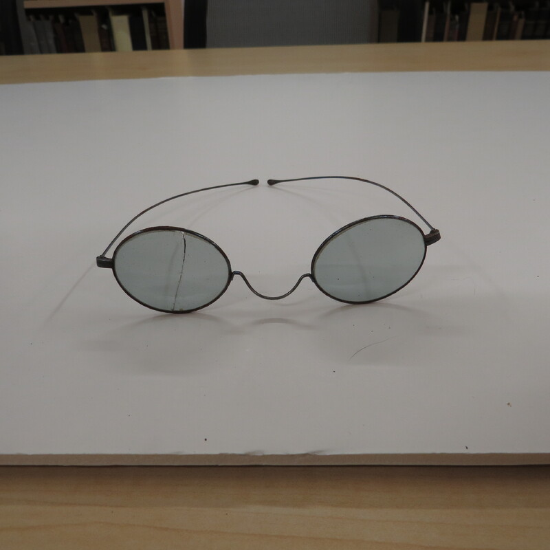 Tinted oval lenses in wire frames with 'W" bridge and straight temporal arms. One lens cracked.