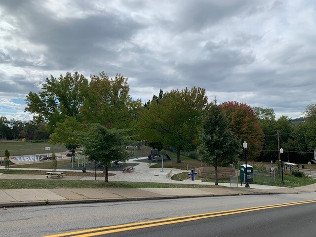 A photograph of a two-lane road on a downward sloping hill with a small park in the background.