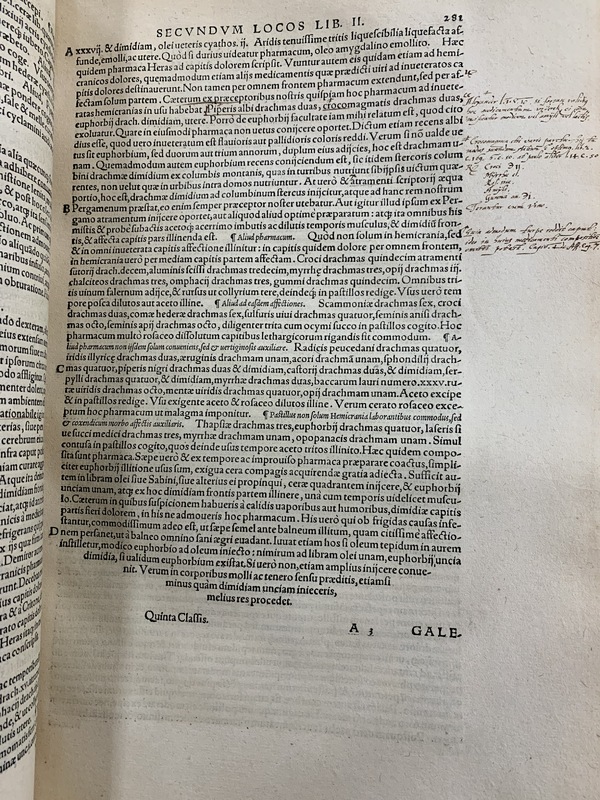 An old book, open to page showing Latin text and handwritten annotations in the left hand margin.
