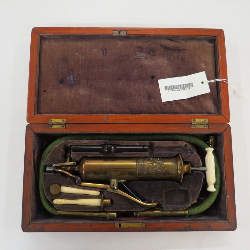 Surgical set. Set includes: 1 combined pump and enema syringe with bone handle and flute key lever, 1 enema tube, 2 oesophageal pipes, vulcanite mouth gag and wooden cap, 2 bone rectum pipes, cylinder attachment for stomach pump/enema apparatus, in wooden case with sage velvet lining and key.