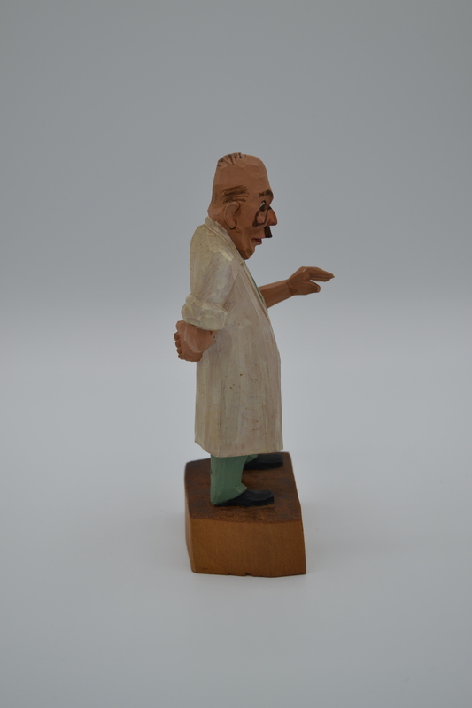 A wood figurine of dentist, holding tooth extracting forceps behind his back,  with inscription: "I'm not heartless, I pull painless" in German