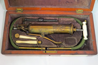 Surgical set. Set includes: 1 combined pump and enema syringe with bone handle and flute key lever, 1 enema tube, 2 oesophageal pipes, vulcanite mouth gag and wooden cap, 2 bone rectum pipes, cylinder attachment for stomach pump/enema apparatus, in wooden case with sage velvet lining and key.